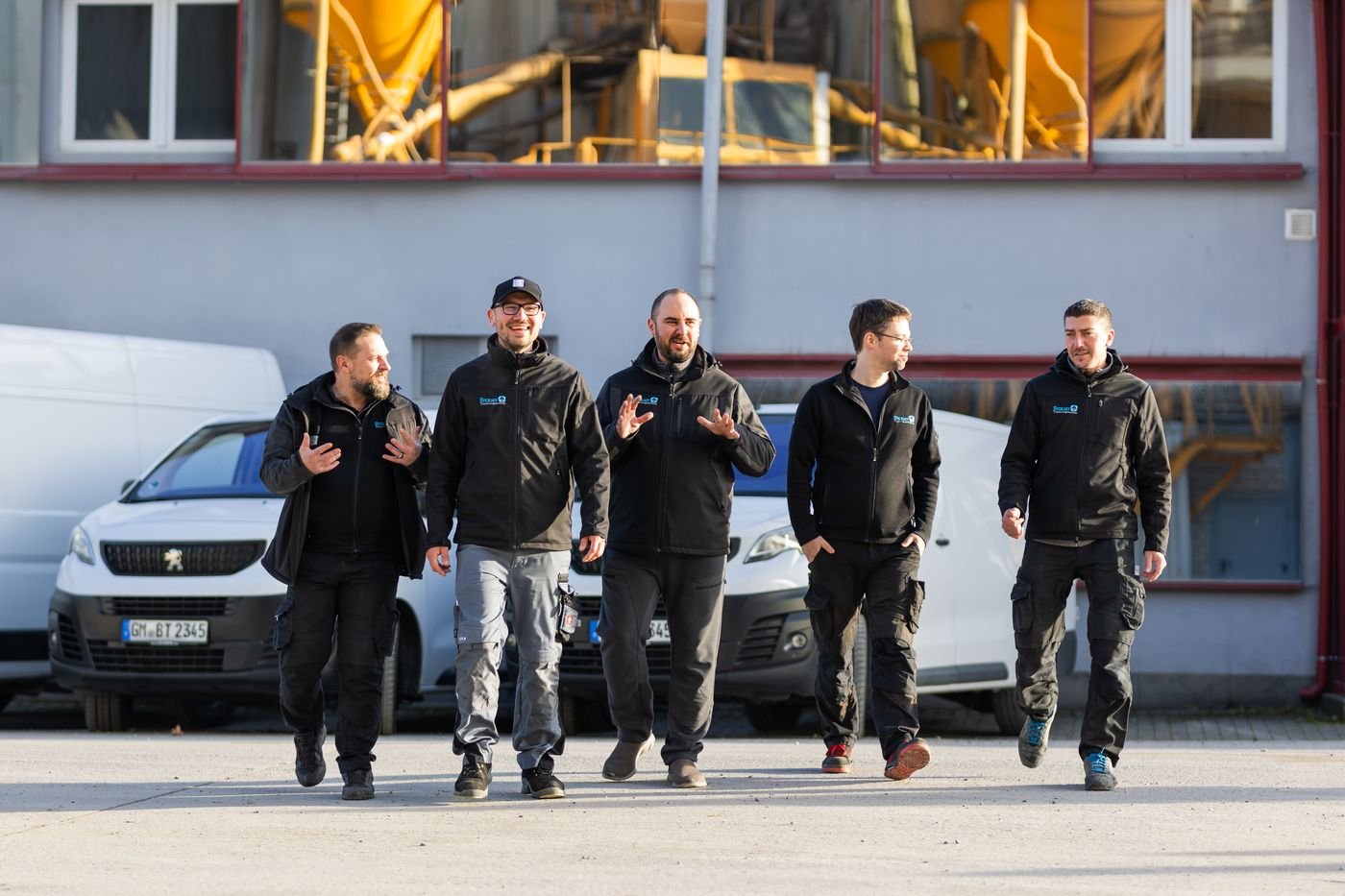 Brauer-Team läuft vor den Firmenfahrzeugen über den Hof